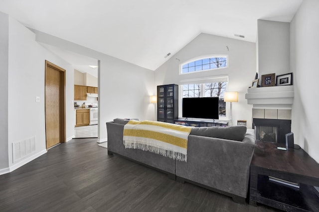 living area featuring high vaulted ceiling, visible vents, dark wood finished floors, and a tile fireplace