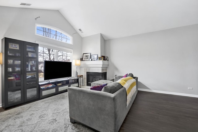 living area featuring high vaulted ceiling, wood finished floors, visible vents, baseboards, and a tiled fireplace