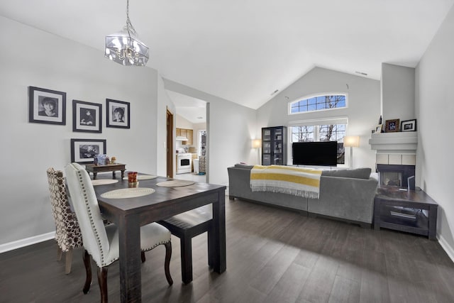 dining area with a chandelier, high vaulted ceiling, wood finished floors, baseboards, and a tiled fireplace