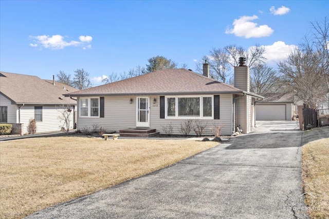 ranch-style home with a shingled roof, a detached garage, a front yard, a chimney, and an outbuilding