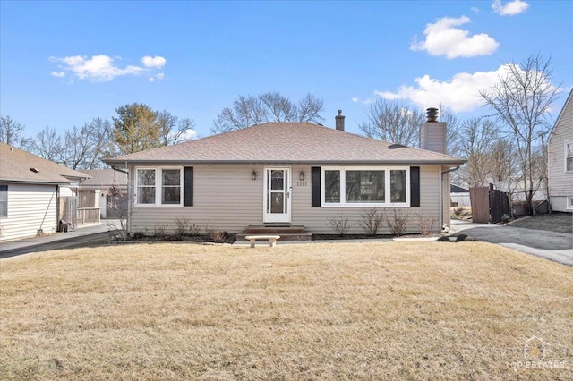 ranch-style home with a front lawn, fence, roof with shingles, and a chimney