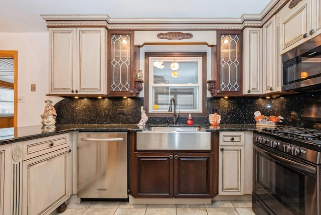 kitchen with stainless steel appliances, tasteful backsplash, cream cabinets, and a sink