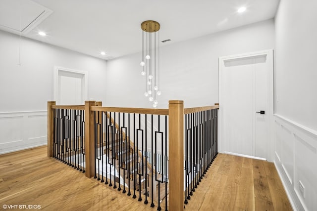 hallway with attic access, a decorative wall, wood finished floors, and an upstairs landing