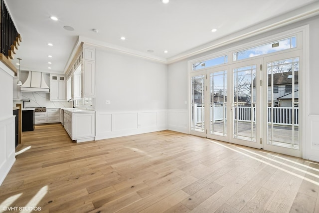 unfurnished living room featuring recessed lighting, a decorative wall, a sink, wainscoting, and light wood-type flooring