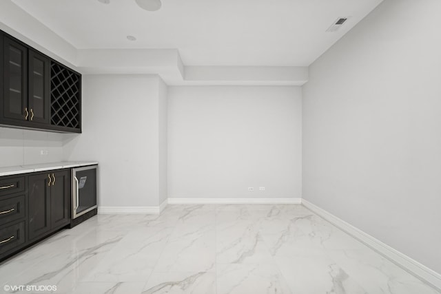 bar with a bar, marble finish floor, wine cooler, and baseboards