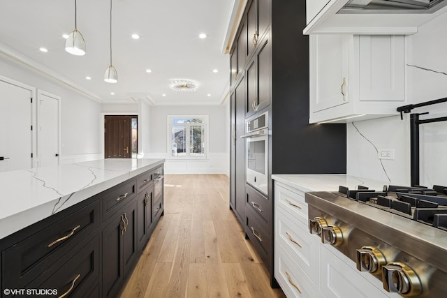 kitchen featuring crown molding, hanging light fixtures, light wood-style flooring, appliances with stainless steel finishes, and wall chimney range hood