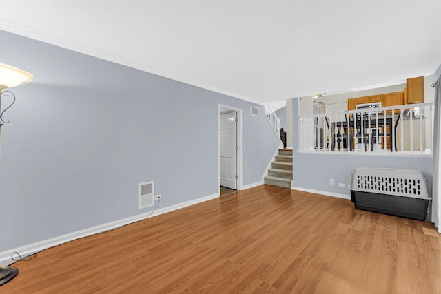 unfurnished living room featuring light wood-type flooring, visible vents, stairway, and baseboards