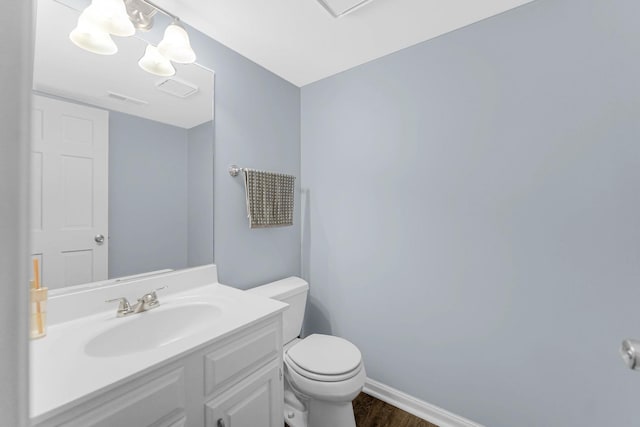 half bathroom with visible vents, toilet, vanity, wood finished floors, and baseboards