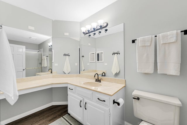 bathroom with toilet, vanity, a shower stall, wood finished floors, and baseboards