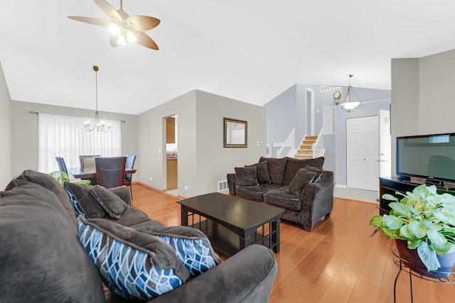 living area with lofted ceiling, ceiling fan with notable chandelier, visible vents, stairway, and light wood finished floors