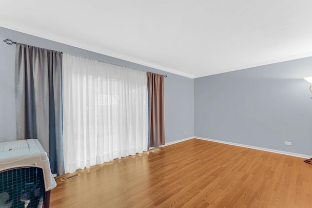 unfurnished living room with ornamental molding, visible vents, baseboards, and wood finished floors