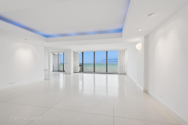 spare room featuring a raised ceiling, floor to ceiling windows, baseboards, and speckled floor