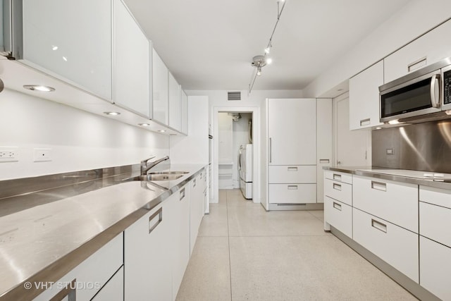 kitchen with stainless steel microwave, stainless steel countertops, white cabinets, independent washer and dryer, and a sink