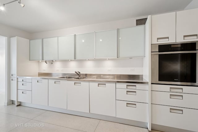 kitchen with stainless steel oven, light speckled floor, stainless steel counters, and a sink