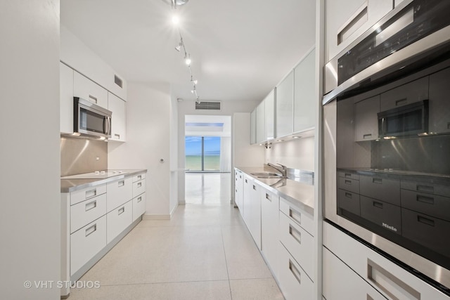 kitchen featuring visible vents, a sink, white cabinets, stainless steel microwave, and modern cabinets