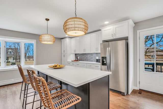 kitchen featuring white cabinets, decorative backsplash, stainless steel fridge with ice dispenser, light wood-style flooring, and a kitchen breakfast bar