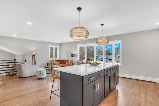 kitchen with light wood-type flooring, a kitchen bar, baseboard heating, and light countertops