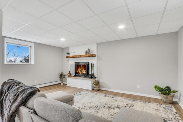 living room featuring a baseboard radiator, a drop ceiling, wood finished floors, and a lit fireplace