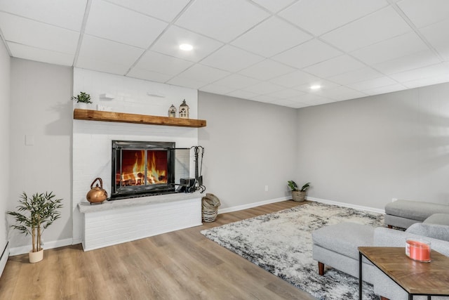 living room featuring a paneled ceiling, a brick fireplace, baseboards, and wood finished floors