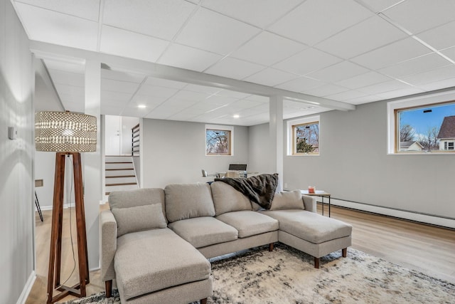 living room with a baseboard radiator, stairs, a drop ceiling, and wood finished floors