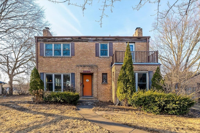 view of front of home with brick siding, a chimney, and a balcony