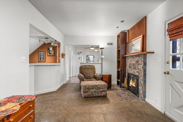 living area featuring a fireplace, visible vents, ceiling fan, dark tile patterned floors, and baseboards