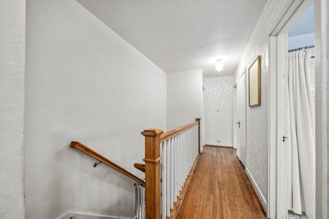 corridor with baseboards, wood finished floors, and an upstairs landing