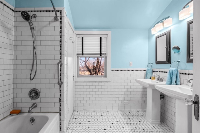 bathroom featuring a wainscoted wall, washtub / shower combination, vaulted ceiling, and tile walls