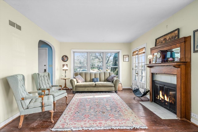 living room featuring arched walkways, a fireplace, visible vents, wood finished floors, and baseboards