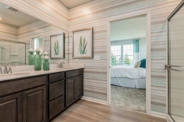 ensuite bathroom with double vanity, wood finished floors, a sink, and a shower with door