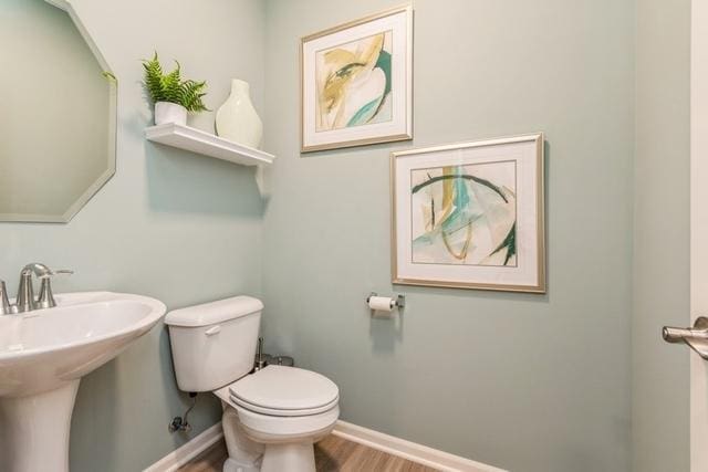 half bath featuring a sink, wood finished floors, toilet, and baseboards