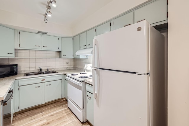 kitchen with under cabinet range hood, white appliances, a sink, light wood-style floors, and tasteful backsplash