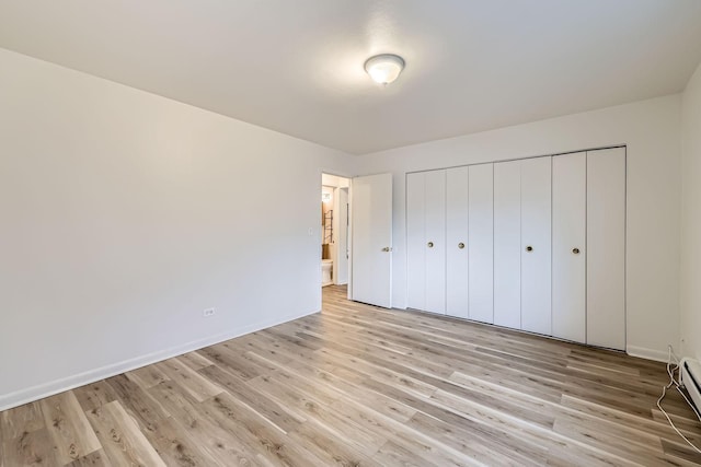 unfurnished bedroom with light wood-type flooring, a baseboard heating unit, baseboards, and a closet