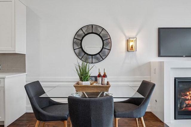 dining space featuring a wainscoted wall, dark wood-style floors, and a glass covered fireplace