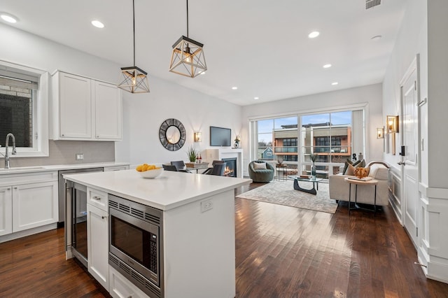 kitchen featuring a warm lit fireplace, dark wood-type flooring, a sink, light countertops, and stainless steel microwave