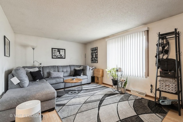 living area featuring visible vents, a textured ceiling, baseboards, and wood finished floors