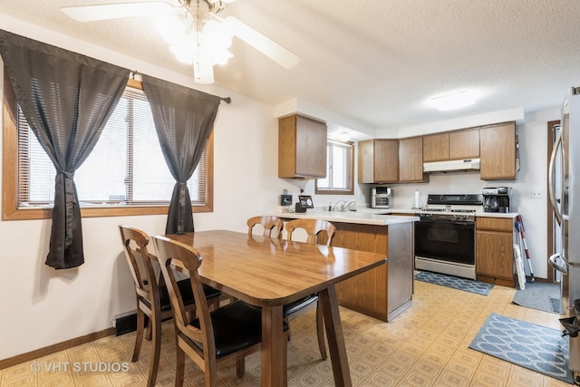 kitchen featuring brown cabinets, a peninsula, light countertops, under cabinet range hood, and gas stove