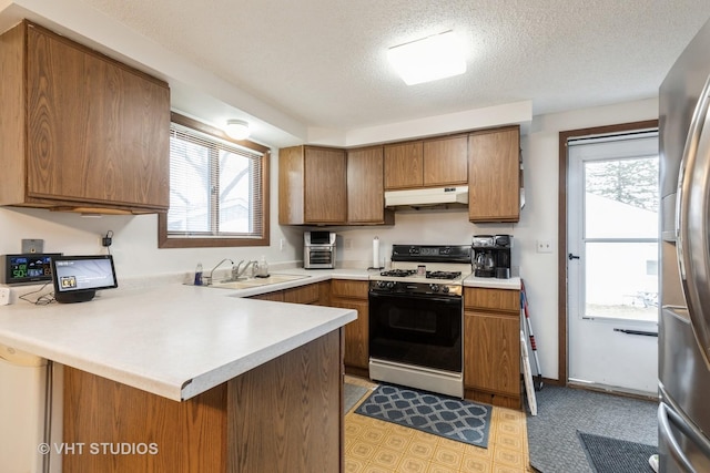 kitchen featuring gas range oven, a healthy amount of sunlight, a peninsula, under cabinet range hood, and stainless steel fridge with ice dispenser