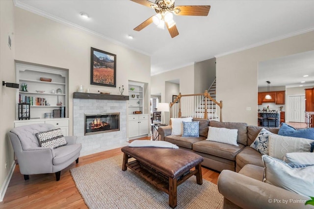 living area with light wood finished floors, ornamental molding, stairs, a brick fireplace, and built in shelves