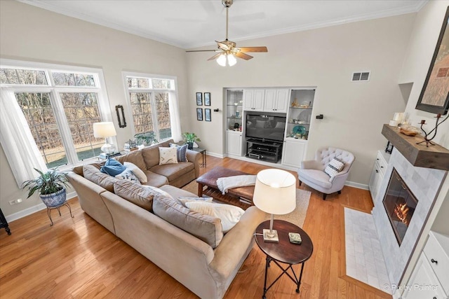 living area with light wood-style floors, a premium fireplace, visible vents, and ornamental molding