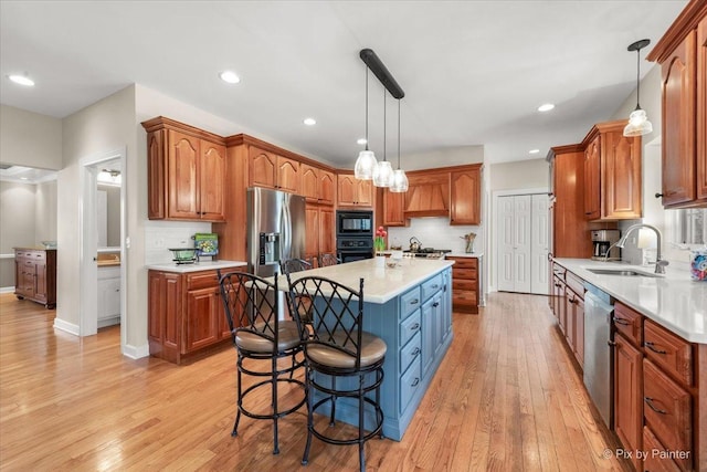 kitchen featuring a center island, light countertops, light wood-type flooring, black appliances, and a sink