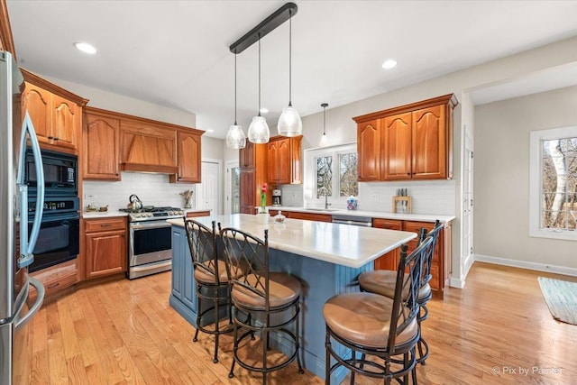 kitchen featuring a kitchen island, light countertops, light wood-type flooring, black appliances, and a kitchen bar