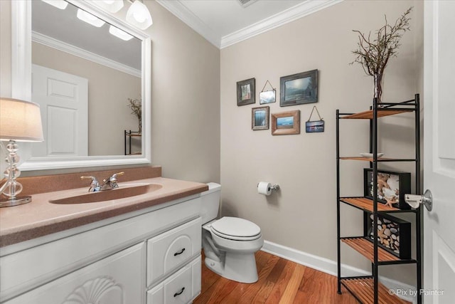 half bathroom with toilet, wood finished floors, vanity, baseboards, and ornamental molding