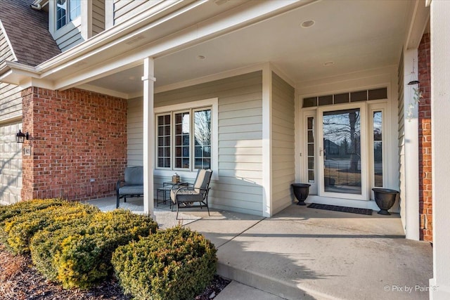 entrance to property featuring covered porch, a shingled roof, and brick siding