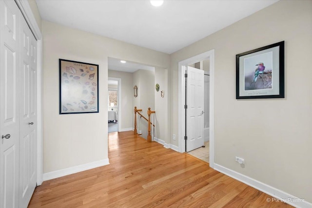 hallway featuring light wood finished floors, an upstairs landing, and baseboards