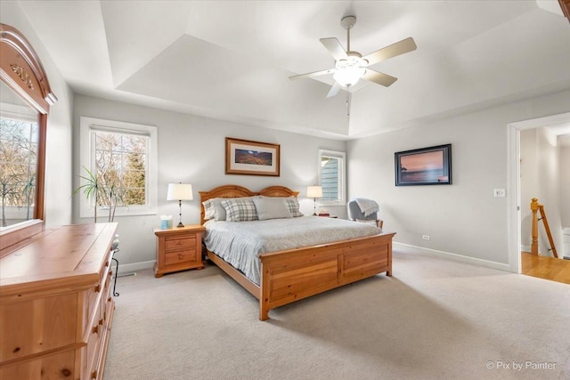 bedroom with baseboards, a raised ceiling, and light colored carpet