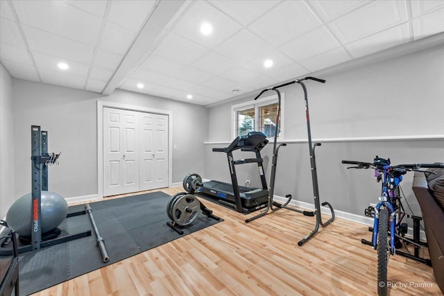 workout area featuring a paneled ceiling, baseboards, wood finished floors, and recessed lighting