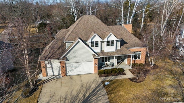 traditional home featuring an attached garage, covered porch, brick siding, a shingled roof, and driveway