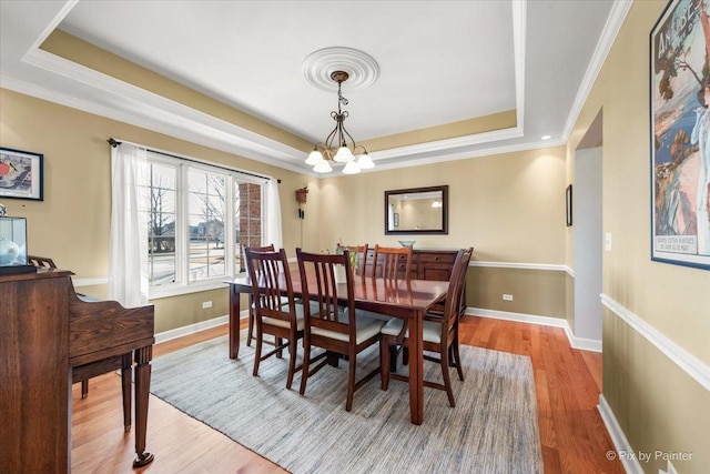 dining space featuring wood finished floors, baseboards, ornamental molding, a tray ceiling, and an inviting chandelier