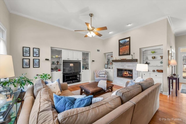 living area featuring a tiled fireplace, light wood-type flooring, and crown molding